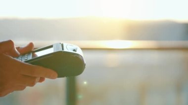 Yakın plan, kadın banka terminalindeki siparişi ödemek için akıllı telefon nakitsiz cüzdan teknolojisi kullanıyor. Kart makinesi erkek eliyle güneş ışığı arkaplanında