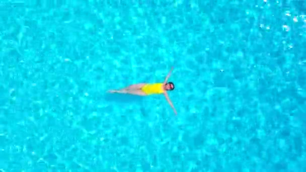En tepeden, havuzda sırtüstü uzanmış sarı mayo giymiş bir kadın görüntüsü. Rahatlatıcı kavram — Stok video