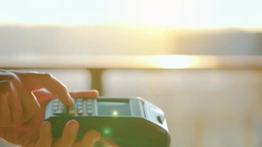Yakın plan, kadın banka terminalindeki siparişi ödemek için akıllı telefon nakitsiz cüzdan teknolojisi kullanıyor. Kart makinesi erkek eliyle güneş ışığı arkaplanında