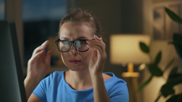 Mulher coloca seus óculos e continua a trabalhar no computador à noite. A tela do monitor é refletida nos óculos. Trabalho remoto — Vídeo de Stock