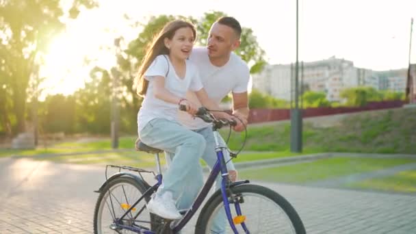 Dad is teaching daughter how to ride bicycle at sunset. Slow motion — Stock Video