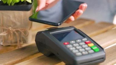Akıllı telefondan yapılan temassız ödeme. Kablosuz ödeme konsepti. Yakın plan, kadın banka terminalindeki siparişi ödemek için akıllı telefon nakitsiz cüzdan teknolojisi kullanıyor..