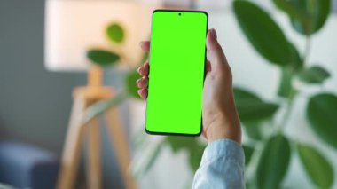 Evde dikey modda yeşil ekranlı akıllı telefon kullanan bir kadın var. Kız internette geziniyor, içeriği izliyor, videolar izliyor. POV.