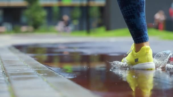 Mulher esportiva correndo ao ar livre, entrando em poça. Um corredor a correr à chuva, a fazer salpicos. Movimento lento — Vídeo de Stock