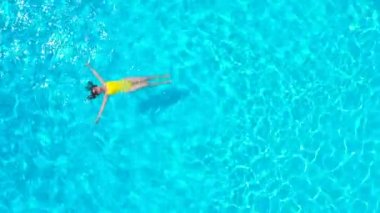 En tepeden, havuzda sırtüstü uzanmış sarı mayo giymiş bir kadın görüntüsü. Rahatlatıcı kavram