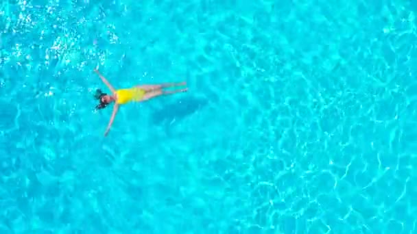 Blick von oben auf eine Frau in einem gelben Badeanzug, die auf dem Rücken im Pool liegt. Entspanntes Konzept — Stockvideo