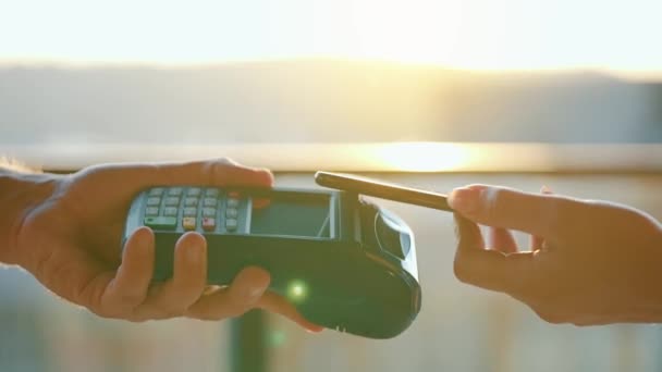 Close-up, woman using smartphone cashless wallet NFC technology to pay order on bank terminal. Card machine in male hand on sunlight background — Stock Video