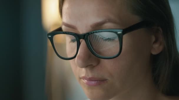 Femme en lunettes regardant sur le moniteur et travaillant avec des graphiques et des analyses. L'écran du moniteur se reflète dans les lunettes. Travailler la nuit. Extrême gros plan — Video