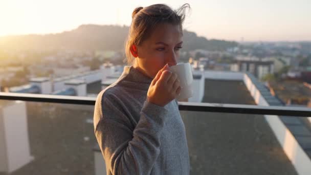 Femme commence sa journée avec une tasse de thé ou de café sur le balcon à l'aube. Paysage urbain en arrière-plan — Video