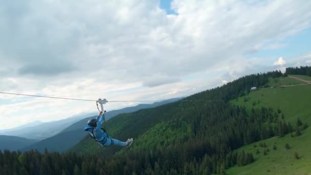 Ungewöhnlicher Anblick einer Frau, die auf einer Seilrutsche zwischen den Bergen reitet. Schneller und wendiger Flug um eine Person herum. Auf FPV-Drohne gefilmt. — Stockvideo