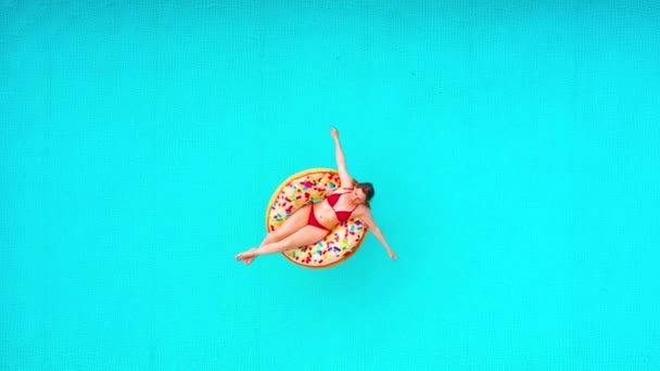 Vista aérea de una mujer en bikini rojo acostada en una dona en la piscina — Vídeos de Stock