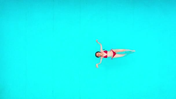 Udsigt fra toppen som en kvinde i rødt badedragt svømmer på ryggen i poolen. Sommer livsstil – Stock-video