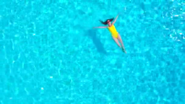 Blick von oben auf eine Frau in einem gelben Badeanzug, die auf dem Rücken im Pool liegt. Entspanntes Konzept — Stockvideo