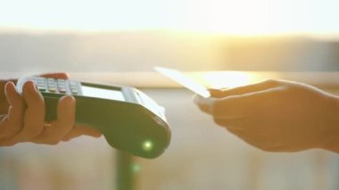 NFC kredi kartı ödemesi. NFC teknolojisiyle kredi kartıyla ödeme yapan bir kadın. Kablosuz para transferi. Kart makinesi erkek eliyle güneş ışığı arkaplanında