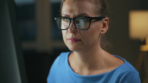 Γυναίκα με γυαλιά που κοιτάει στην οθόνη και σερφάρει στο ίντερνετ. Η οθόνη της οθόνης αντανακλάται στα γυαλιά. Δουλειά τη νύχτα. Γραφείο Εσωτερικών. Απομακρυσμένη εργασία — Αρχείο Βίντεο