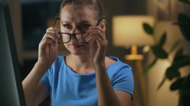 Μια γυναίκα φοράει τα γυαλιά της και συνεχίζει να δουλεύει στον υπολογιστή τη νύχτα. Η οθόνη της οθόνης αντανακλάται στα γυαλιά. Απομακρυσμένη εργασία — Αρχείο Βίντεο