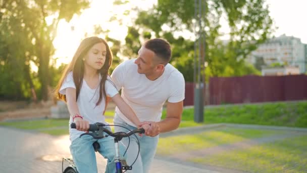 O pai está a ensinar a filha a andar de bicicleta ao pôr-do-sol. Movimento lento — Vídeo de Stock