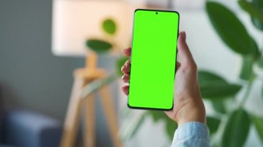 Evde dikey modda yeşil ekranlı akıllı telefon kullanan bir kadın var. Kız internette geziniyor, içeriği izliyor, videolar izliyor. POV.