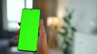 Evde dikey modda yeşil ekranlı akıllı telefon kullanan bir kadın var. Kız internette geziniyor, içeriği izliyor, videolar izliyor. POV.