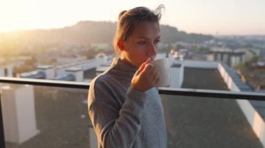 Kadın güne şafakta balkonda bir fincan çay ya da kahveyle başlıyor, ağır çekimde. Arka planda şehir manzarası