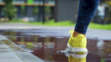 Bayan sporcu kadın dışarıda koşuyor, su birikintisine giriyor. Yağmurda koşan tek koşucu, su sıçratıyor. Yavaş çekim