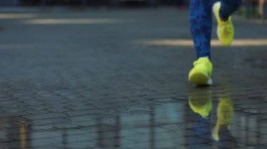 Bayan sporcu kadın dışarıda koşuyor, su birikintisine giriyor. Yağmurda koşan tek koşucu, su sıçratıyor. Yavaş çekim