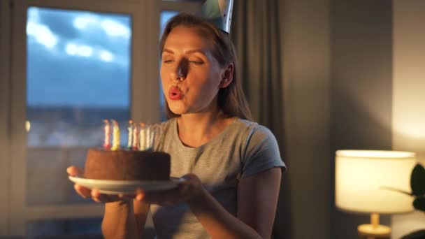 Счастливая взволнованная женщина загадывает заветное желание и раздувает свечи на праздничном торте, празднуя день рождения дома, замедляет ход — стоковое видео