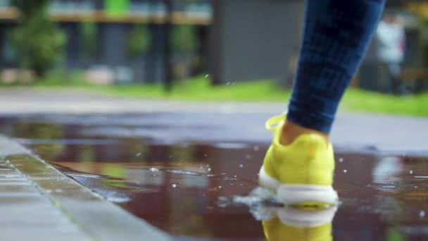 Mulher esportiva correndo ao ar livre, entrando em poça. Um corredor a correr à chuva, a fazer salpicos. Movimento lento — Vídeo de Stock