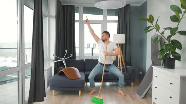 男は家を掃除し、楽しいダンスをし、ほうきで歌う — ストック動画