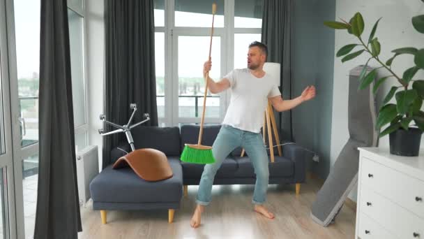 Een man die het huis schoonmaakt en plezier heeft met dansen en zingen met een bezem. Langzame beweging — Stockvideo