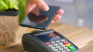 Akıllı telefondan yapılan temassız ödeme. Kablosuz ödeme konsepti. Yakın plan, kadın banka terminalindeki siparişi ödemek için akıllı telefon nakitsiz cüzdan teknolojisi kullanıyor..