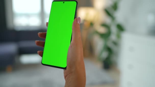 Kvinna hemma med hjälp av smartphone med grön mock-up skärm i vertikalt läge. Flicka surfa på Internet, titta på innehåll, videor. Födelsedatum. — Stockvideo