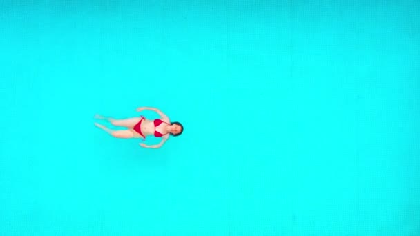 Vista desde la parte superior como una mujer en traje de baño rojo nada sobre su espalda en la piscina. Estilo de vida — Vídeos de Stock