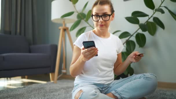 안경을 쓴 여성 이 바닥에 앉아 신용 카드와 스마트폰으로 온라인 구매를 하고 있습니다. 온라인 쇼핑, 생활 방식 기술 — 비디오