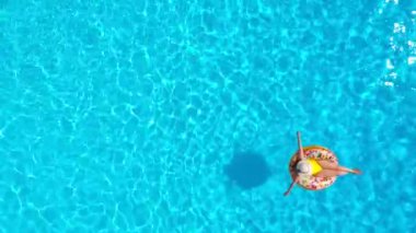 Havuzda donutun üzerinde yatan sarı mayo giymiş bir kadının hava manzarası.