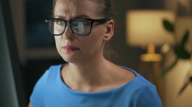 Gözlüklü kadın monitöre bakıyor ve internette sörf yapıyor. Monitör ekranı gözlüklere yansıyor. Gece çalış. İçişleri Bakanlığı. Uzak çalışma