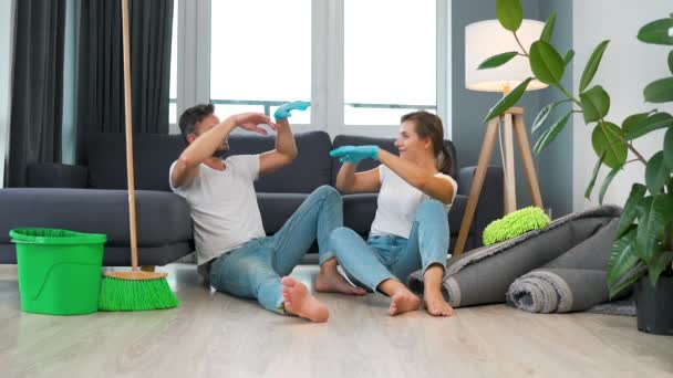 Casal cansado senta-se no chão em uma sala e alta cinco uns aos outros depois que eles terminam de limpar a casa. Movimento lento — Vídeo de Stock