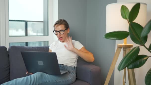 Lässig gekleidete Frau mit Brille sitzt auf dem Sofa und kommuniziert per Videoverbindung mit Familie oder engen Freunden — Stockvideo