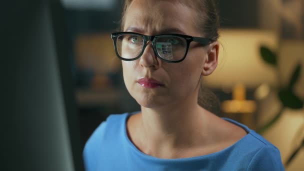 Frau mit Brille blickt auf den Monitor und surft im Internet. Der Monitor-Bildschirm spiegelt sich in der Brille wider. Arbeiten in der Nacht. Innenministerium. Fernbedienung — Stockvideo