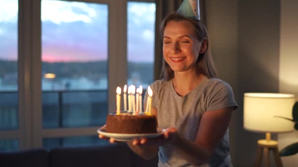 Feliz mulher animada fazendo desejo estimado e soprando velas no bolo de férias, comemorando o aniversário em casa — Vídeo de Stock