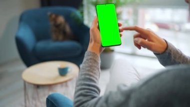 Evde dikey modda yeşil ekranlı akıllı telefon kullanan bir kadın var. Kız internette geziniyor, içeriği izliyor, videolar izliyor. POV.