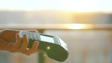 NFC kredi kartı ödemesi. NFC teknolojisiyle kredi kartıyla ödeme yapan bir kadın. Kablosuz para transferi. Kart makinesi erkek eliyle güneş ışığı arkaplanında