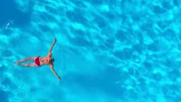 Blick von oben, als eine Frau im roten Badeanzug im Pool schwimmt. Sommerlicher Lebensstil — Stockvideo