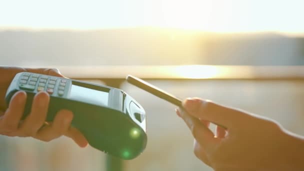 Close-up, mujer que utiliza teléfono inteligente billetera sin efectivo tecnología NFC para pagar la orden en la terminal bancaria. Máquina de tarjetas en mano masculina sobre fondo de luz solar — Vídeos de Stock