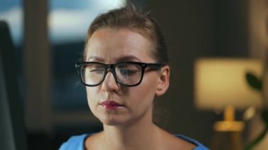 Gözlüklü kadın monitöre bakıyor ve internette sörf yapıyor. Monitör ekranı gözlüklere yansıyor. Gece çalış. İçişleri Bakanlığı. Uzak çalışma