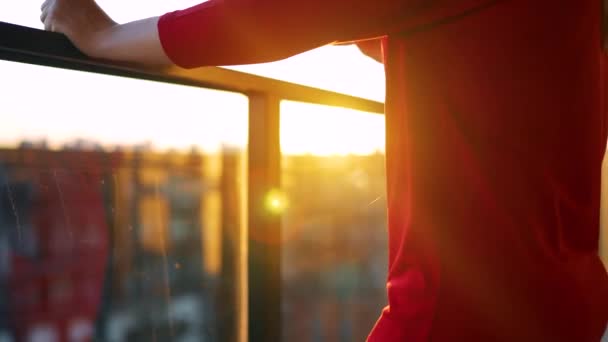 Женщина в красном платье с чашкой кофе, стоящей на балконе и любующейся закатом. Медленное движение — стоковое видео