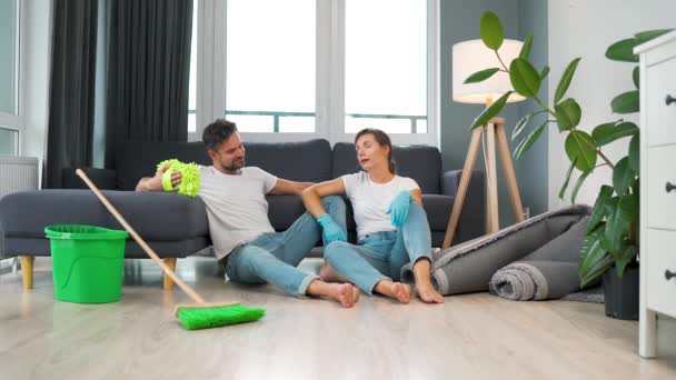 Couple fatigué est assis sur le sol dans une pièce et cinq haut l'un l'autre après avoir terminé le nettoyage de la maison. Mouvement lent — Video