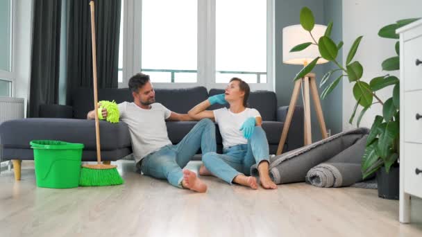 Couple fatigué est assis sur le sol dans une chambre et cinq haut l'un l'autre après avoir terminé le nettoyage de la maison. — Video