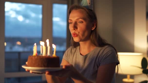Щаслива збуджена жінка робить заповітні бажання і дме свічки на святковий торт, святкуючи день народження вдома — стокове відео