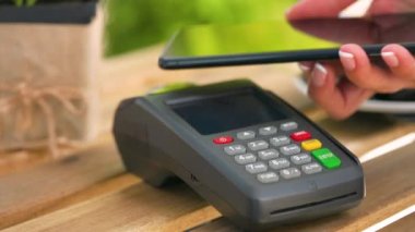 Akıllı telefondan yapılan temassız ödeme. Kablosuz ödeme konsepti. Yakın plan, kadın banka terminalindeki siparişi ödemek için akıllı telefon nakitsiz cüzdan teknolojisi kullanıyor..